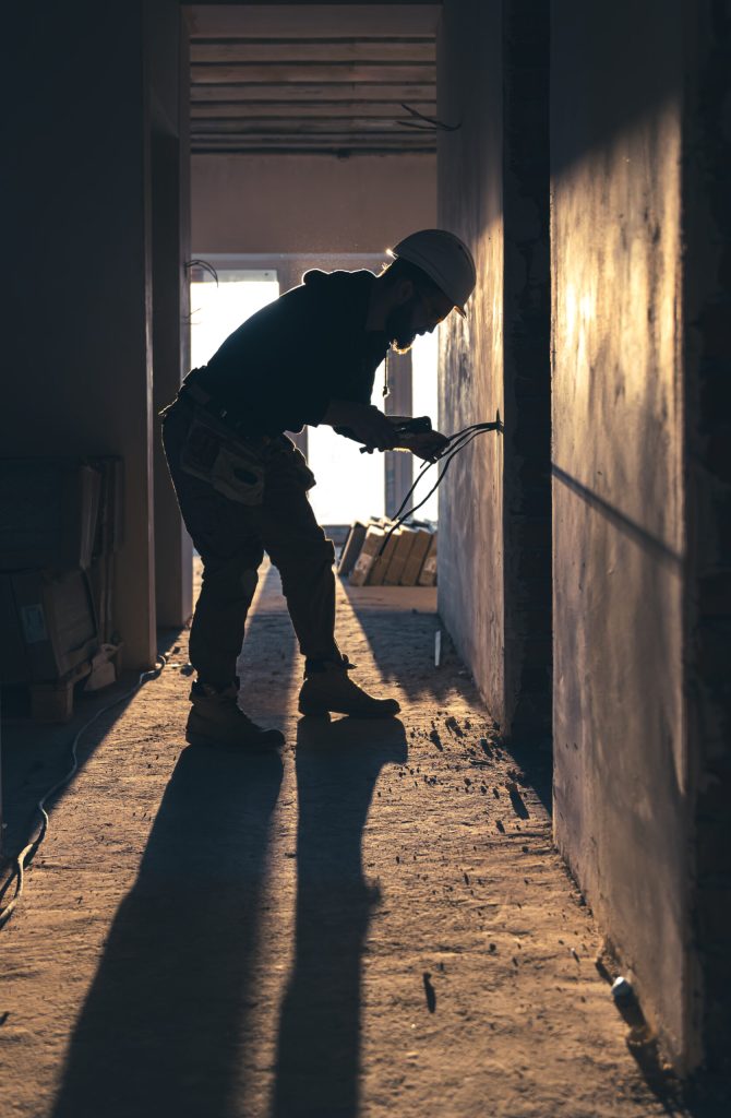 A construction electrician cuts a voltage cable during a repair, silhouette in the light of the setting sun.